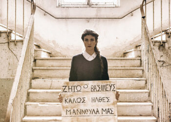 Μία γυναίκα κρατά μια επιγραφή που γράφει "Ζήτω ο Βασιλεύς. Καλώς ήλθες Μαννούλα μας"