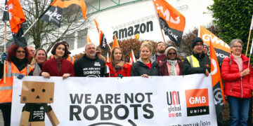 Εργαζόμενοι διαδαηλώνουν έξώ από κτήριο της Amazon με πανό που γράφει "Δεν είμαστε ρομπότ"